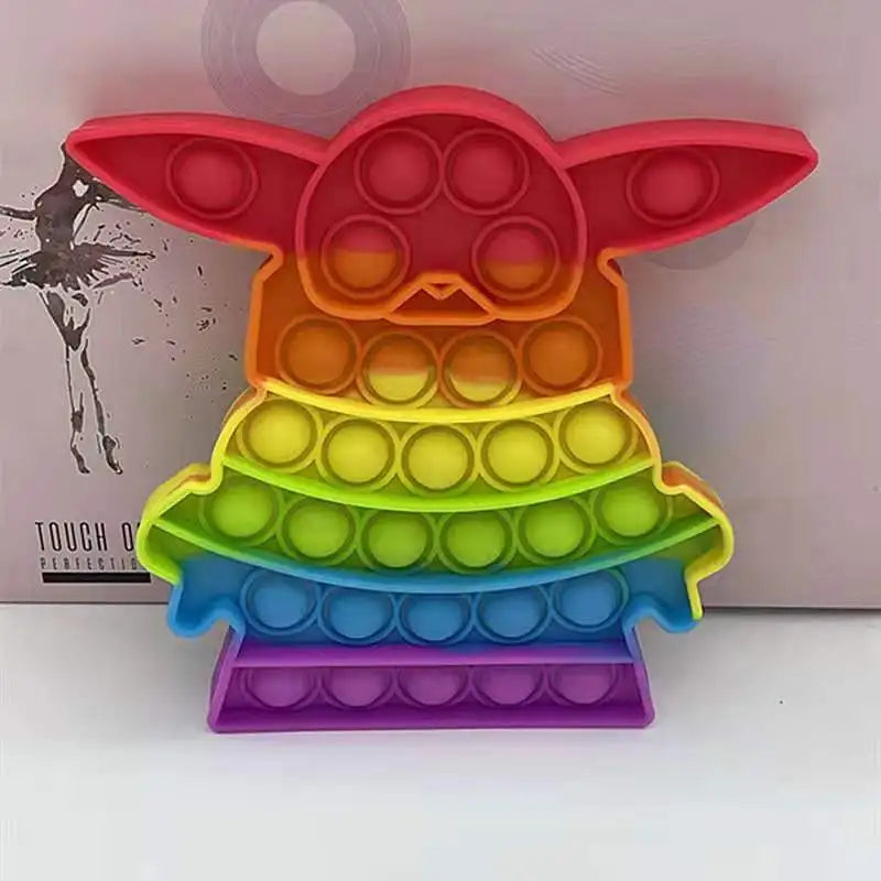 FidgetFuns Rainbow Pop Fidget Stress Toy is an abstract creature-shaped pop-it with large ears, offering sensory satisfaction. It features circular bubbles in gradient colors from red to purple placed against a plain backdrop.